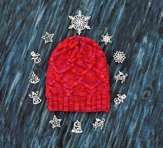 a red knitted hat sitting on top of a wooden table next to snowflakes