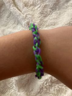 a person wearing a purple and green braided bracelet on their left arm, with one hand holding the other