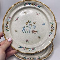 two plates with flowers and people painted on them are being held by a woman's hand