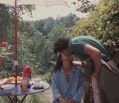 two people kissing each other in front of an umbrella and table with food on it