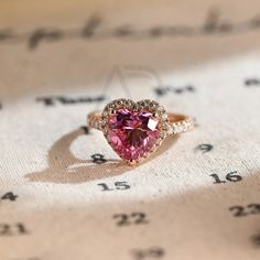 a pink heart shaped diamond ring sitting on top of a piece of paper with numbers in the background