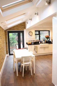 a dining room table and chairs in front of an open kitchen area with skylights