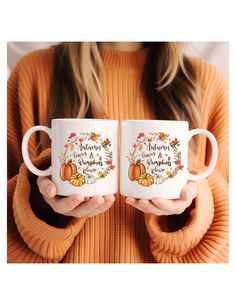 a woman holding two coffee mugs in her hands with autumn leaves and pumpkins on them