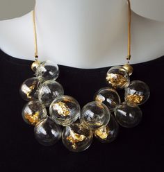 Unique and chic, This Glass beads bib necklace, for sure is a conversation starter. This Clear and Gold bubbles statement necklace combines transparent hollow glass beads, Filled with pieces of 22 karat gold leaf, in a cluster shape, connected to a Leather cord, and closes with a goldfilled clasp. The necklace has 2 inches (5 cm) chain to adjustable length. You can pair this unique necklace with these earrings: https://etsy.me/3Qg86lX This bold-blown airy jewelry is light and easy to wear, Perfe Luxury Handmade Clear Necklace, Luxury Adjustable Glass Necklace, Modern Glass Necklaces For Formal Occasions, Modern Glass Necklaces For Formal Events, Handmade Gold Bib Necklace For Parties, Unique Glass Necklace For Parties, Modern Handmade Necklaces For Party, Gold Bib Necklace With Round Beads For Parties, Gold Glass Necklaces For Formal Occasions