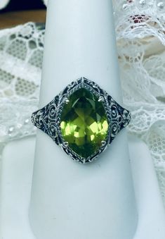 Natural Green Peridot Ring Iris Design#201 Custom Made This is a stunning Art Deco vintage reproduction ring in sterling silver filigree with a 3.12 carat Natural green peridot gemstone. The brilliant natural gem is 13mm in long by 9mm wide. The ring is 17mm North-South on the finger. The inside of the band is marked 925 for solid sterling silver. This is a lovely reproduction of a vintage antique filigree ring. There is beautiful craftsmanship evidenced in the silver filigree setting. See the f Classic Green Gemstone With Center Stone, Classic Green Gemstones With Accents, Art Deco Green Jewelry With Round Cut, Art Deco Green Round Cut Jewelry, Classic Green Marquise Rings, Classic Peridot Jewelry With Accent Stones, Green Gemstone Ring With Marquise Cut, Green Marquise Cut Gemstone Ring, Green Marquise Rings With Accent Stones