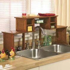 a kitchen sink sitting under a window next to a wooden shelf filled with clutter