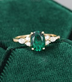 an emerald colored ring with three white diamonds on the band and in front of a green velvet bag