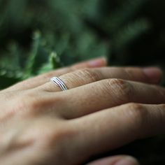 a person's hand with a wedding ring on top of their finger, surrounded by greenery