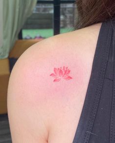 a woman's shoulder with a small pink flower tattoo on it