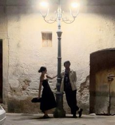 a man and woman standing next to a lamp post in an alleyway at night