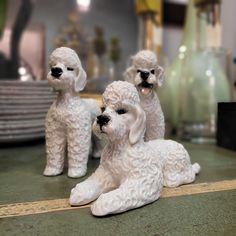 three white poodle figurines sitting on top of a counter next to plates