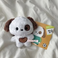 a white stuffed animal with brown ears and nose sitting next to a book on a bed