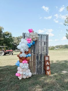 balloons are arranged on the back of a wooden fence for an outdoor baby shower party