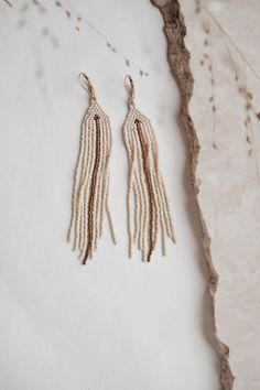 Add a touch of understated elegance with these delicate gold and linen glass bead earrings.  The beautiful, handwoven glass beads in a soft, warm linen color are complemented by delicate silver 24k gilded hooks, creating a timeless and versatile piece.  Lightweight and comfortable to wear, these earrings are perfect for dressing up or adding a touch of sophistication to your everyday look. Materials: Glass beads (linen and gold color), silver 24k gilded hypoallergenic hooks  Dimensions: length 4 inches, width 0,6 inches (10cm x 1cm) Seed Bead Fringe Earrings, Bead Fringe Earrings, Bead Fringe, Glass Bead Earrings, Symbolic Jewelry, Snake Earrings, Made Jewelry, Beaded Fringe, Seed Bead Earrings