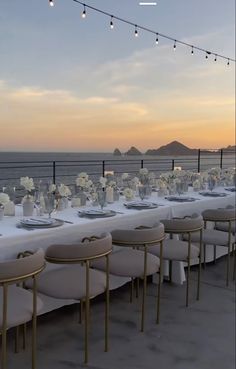 a long table set up with white linens and place settings for dinner on the beach