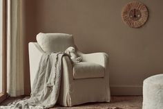 a white chair with a blanket on it next to a window and a wall clock