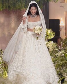 a woman in a white wedding gown and veil walking down the runway with flowers around her