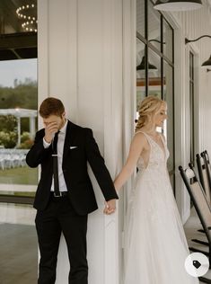 a bride and groom standing next to each other in front of a white wall holding hands