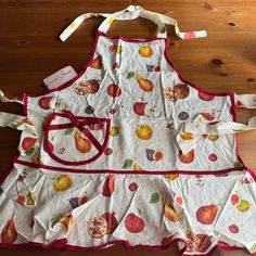 an apron with apples on it sitting on top of a wooden table next to scissors