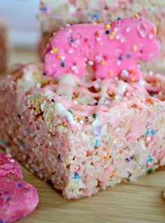 a piece of cake with pink frosting and sprinkles on it sitting on a wooden table