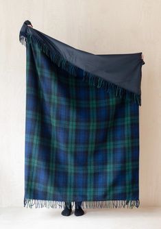 a blue and green plaid blanket with fringes on the end, hanging from a wall