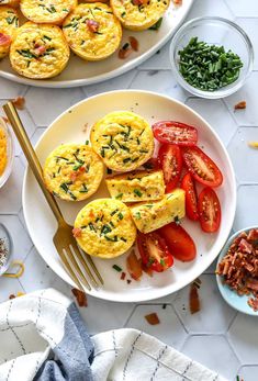 two plates filled with eggs, tomatoes and spinach on top of a white table