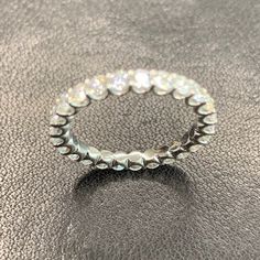 a silver ring sitting on top of a black leather surface with lots of small white stones