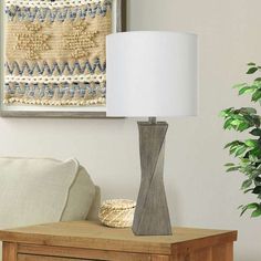 a table lamp sitting on top of a wooden dresser next to a white pillow and potted plant