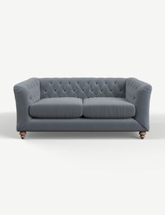 a grey couch with wooden legs and buttons on the back, in front of a white background