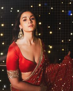 a woman in a red sari and gold jewelry poses for the camera with lights behind her