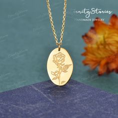 a gold necklace with a rose engraved on the front and back, sitting next to a yellow flower