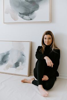 a woman is sitting on the floor in front of two paintings and posing for a photo