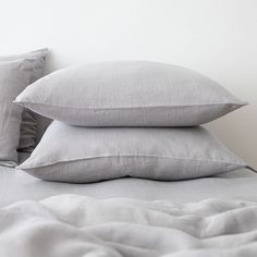 three pillows are stacked on top of each other in front of a white wall and bed