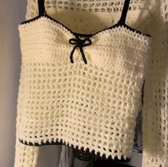 a white crocheted sweater hanging on a wall with a black tie around the neck