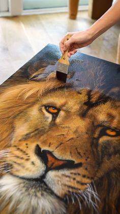 a person is painting a lion on a canvas with a paintbrush in their hand