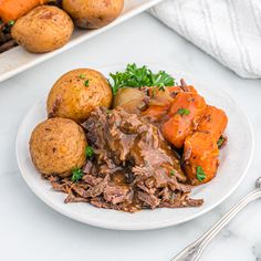 a white plate topped with meat, potatoes and carrots next to other food items