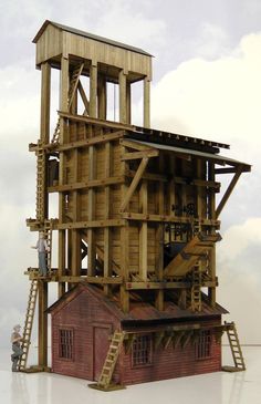 a model of a house made out of wooden planks and wood slats with a man standing on the roof