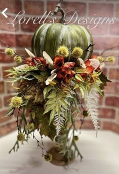 a vase filled with lots of flowers and greenery on top of a white table