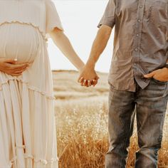 a pregnant couple holding hands in a field