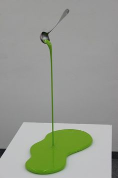 a spoon sticking out of the top of a green liquid drop on a white surface