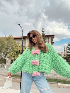 a woman is wearing a green sweater with pink bows and holding a white purse in her hand