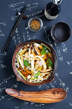 a bowl of soup with chopsticks and seasoning next to it on a table