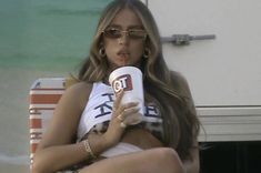 a woman sitting on a beach chair with a drink in her hand and wearing sunglasses