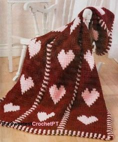 a crocheted blanket with hearts on it is laying on the floor next to a rocking chair