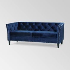 a blue velvet couch with studding on the arms and back, in front of a white background