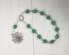 "This set of Mokosh prayer beads consists of a loop of twelve beads; joining the string is an additional bead and a pendant, a symbol representing the goddess: a spider's web, a reminder of her role as goddess of spinning and weaving. It is made with 10mm deep green fire-polished glass beads, separated by silver-toned metal spacer beads, and glass seed beads to provide a comfortable transition from one bead to the next and to make the piece lightweight, supple, and easy to handle. The string its Faceted Spiritual Beads For Gifts, Green Spiritual Bead Bracelet, Spiritual Faceted Bead Bracelet, Bohemian Rosary Bracelet With Faceted Beads As Gift, Traditional Rosary Bracelet With 8mm Beads As Gift, Bohemian Rosary Bracelet With Faceted Beads, Green Faceted Spiritual Beads, Hand-strung Amulet Beads For Gifts, Hand-strung Amulet Beads As Gifts