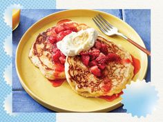 pancakes with strawberries and whipped cream on a yellow plate next to a glass of orange juice