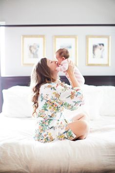 a woman sitting on top of a bed holding a baby in her arms and kissing her cheek