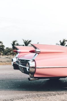 an old pink car parked on the side of the road with palm trees in the background