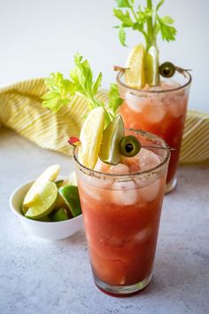 two glasses filled with drinks and garnished with limes, olives and cilantro